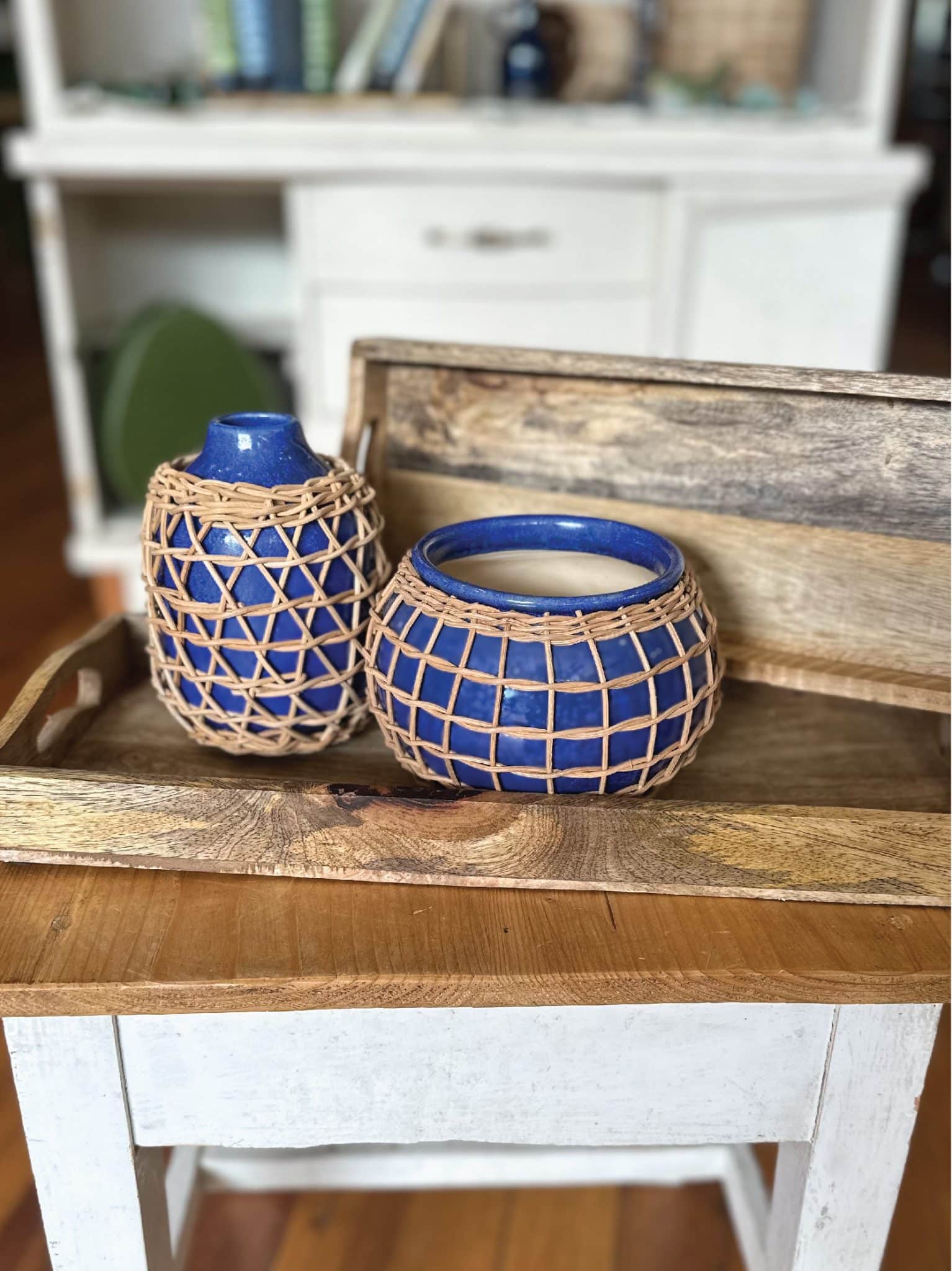 The Rattan Planter & Vase. Both rich indigo blue glaze, wrapped in handwoven rattan for added texture and style. Perfect for cottage, vintage, and boho chic decor. Styled with wooden trays. Showing top angle.