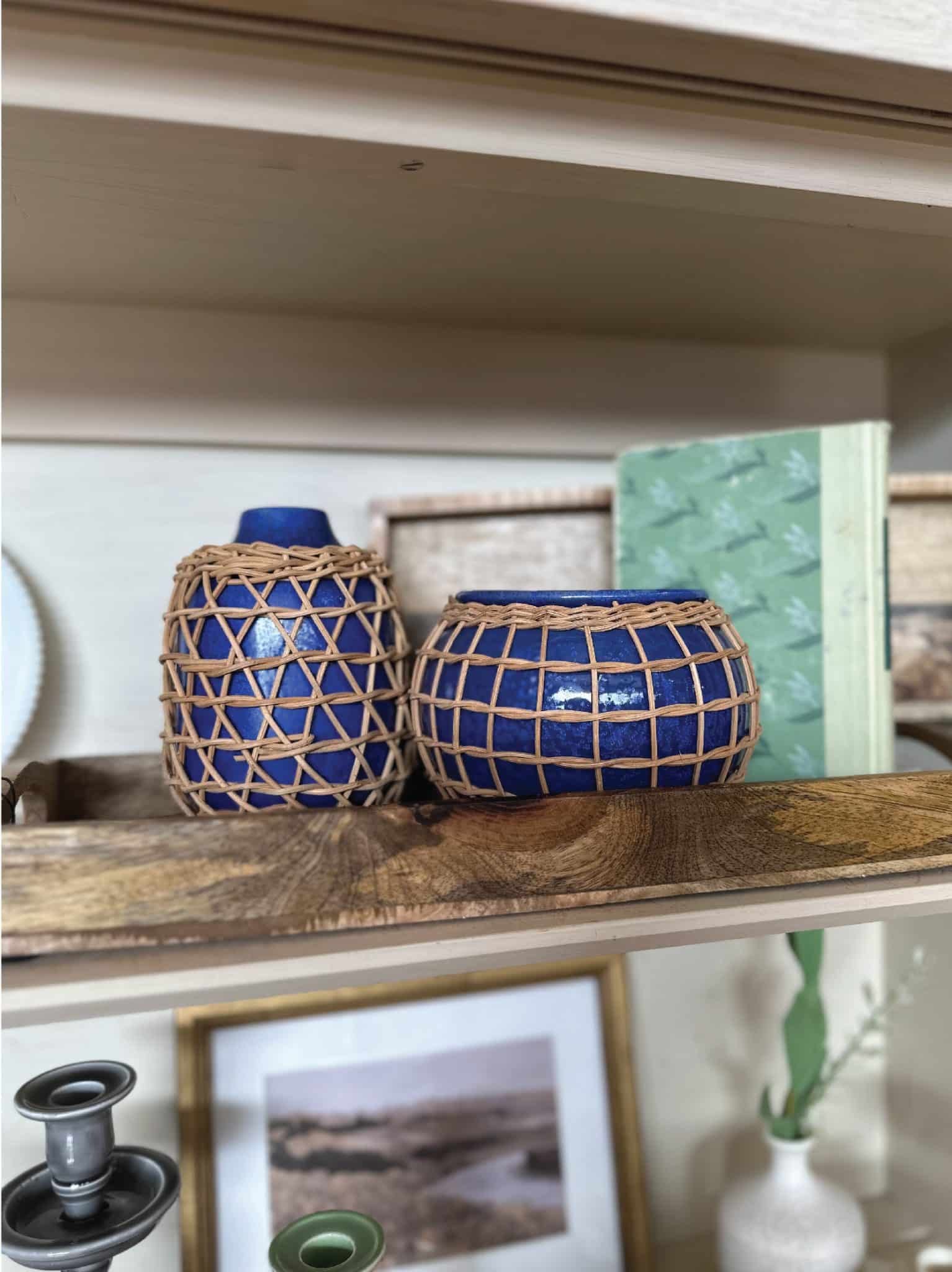 The Rattan Planter & Vase. Both rich indigo blue glaze, wrapped in handwoven rattan for added texture and style. Perfect for cottage, vintage, and boho chic decor. Styled with wood trays in a hutch.