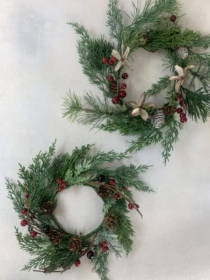 Flat lay of two mini holiday wreaths with pine, berries, and cones.