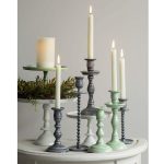 A mix of taper candle holders featuring Small and Medium Mint Empire, Gray Empire, and Off-White Pedestal styles, all glowing with lit candles and accented by soft greenery.