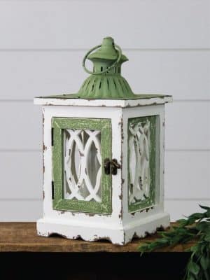 Cottage chic lantern in distressed white and green with vintage latch, scalloped base, and metal top with handle, perfect for farmhouse and cottage-style decor.